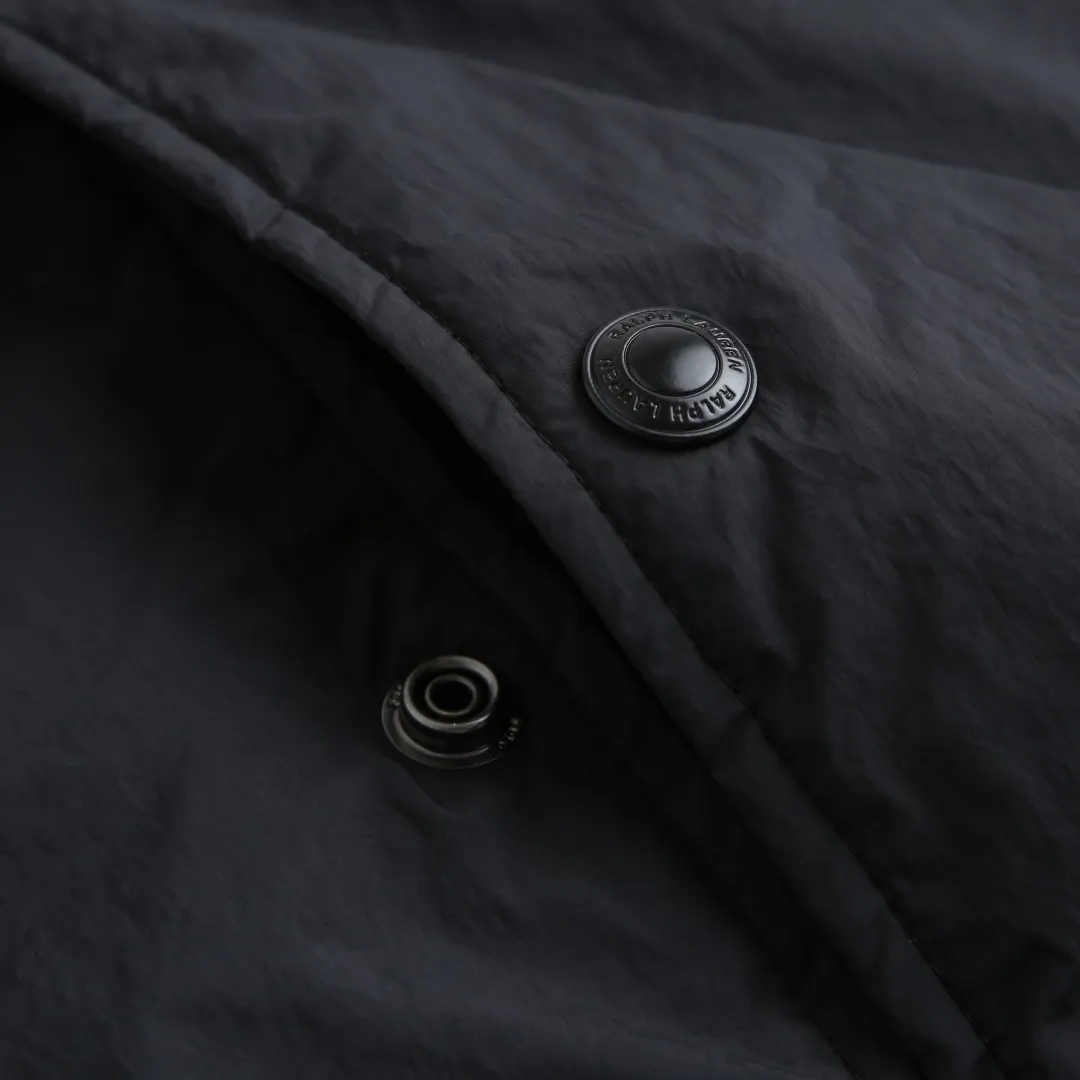 P650 Ralph Lauren pony embroidered light cotton jacket. The fabric is made of high-density nylon taffeta fabric, which combines pragmatism and classic texture. The density is about 210T-300T, the surface is smooth and slightly matte, it has excellent windproof and waterproof properties (with DWR water-repellent treatment), it has strong wrinkle resistance and is easy to care for, which is in line with the positioning of American casual "durable and practical". Classic dark black, using vat dyeing process (dye penetrates into the fiber), the color fastness reaches ISO level 4 or above, preventing fading or color transfer after washing. The lining is made of light cotton-polyester blended fabric (65% Polyester + 35% Cotton) to reduce the friction between the fabric and the inner clothing and improve the smoothness of wearing; the blended material has both breathability and durability to avoid the stuffy feeling of pure nylon lining. The style is a loose fit of the classic Coach Jacket, with slightly dropped shoulder lines (shoulder width is 1-2cm wider than the standard fit). The length reaches the hips, and the sleeves are slightly tapered straight sleeves, taking into account both freedom of movement and casual style. The Polo horse logo on the left chest is flat satin stitch embroidery (satin embroidery). Embroidery thread: 100% polyester high color fastness embroidery thread (the color number is consistent with the brand’s standard red color card). The stitch density is 12-15 stitches/cm. The outline of the horse logo is clear, and the details of the rider and horse are burr-free. The embroidery is positioned accurately through the template (12cm from the bottom of the neckline and 8cm from the placket) to ensure left-right symmetry and centering. The seams of the body are made of double-needle flat seams (needle pitch 3cm/10 needles), the stitches are flat and straight, the stitching color is dark black (the same color as the fabric), and the stitch width is 0.5cm, which enhances firmness while forming simple decorative lines. The front placket is spliced ​​with the body. The placket is made of double-layer folding + flat seam splicing. The thickness is about 0.3cm to ensure that the buttons are not easily deformed when fixed. The edges of the placket are cut with a hot knife to avoid burrs. The armholes where the sleeves and body are joined are made with round-head keyhole machine seams + flat seams. After splicing, the armholes have a natural curvature and no sense of tightness during movement. The height of the sleeves is about 8-10cm, which is in line with the loose characteristics of casual jackets. The main buttons are made of black urea resin buttons with a matte surface. The button holes are hand-made keyholes (6 strands of cotton thread, keyhole density of 8 stitches/mm), and the edges of the eyelets are smooth and without burrs. The first button on the neckline is a hidden button (diameter 12mm), which prevents the neckline from opening and improves the neatness of wearing. Size:S-M-L-XL